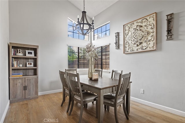 dining room featuring an inviting chandelier, high vaulted ceiling, baseboards, and wood finished floors