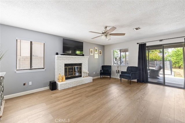 living room with a fireplace, a textured ceiling, visible vents, and light wood-type flooring