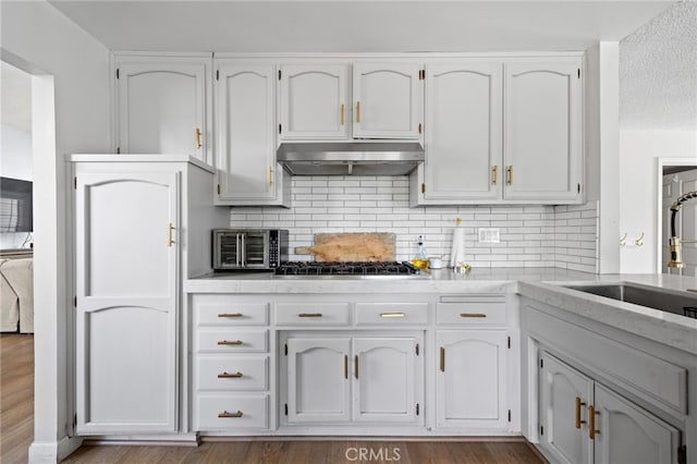 kitchen with wood finished floors, backsplash, under cabinet range hood, and white cabinets