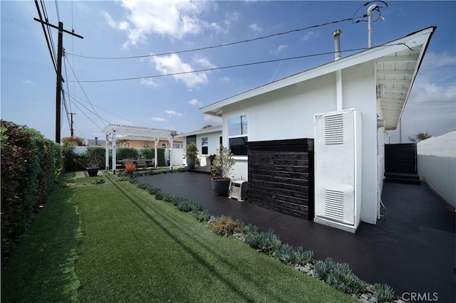 view of side of property with fence, a pergola, stucco siding, and a lawn
