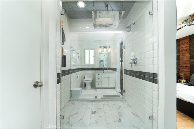 bathroom featuring tile walls, a shower stall, vanity, toilet, and marble finish floor