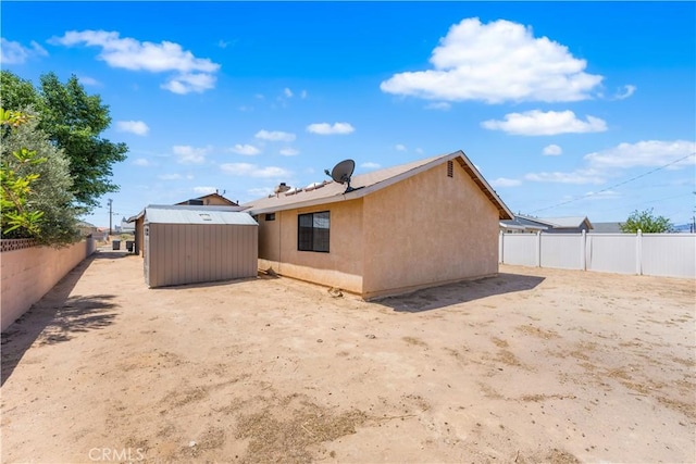 rear view of property with a storage shed, an outdoor structure, a fenced backyard, and stucco siding