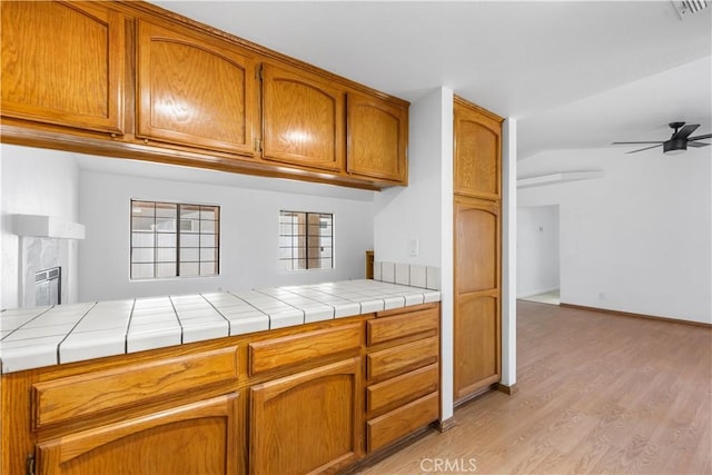 kitchen with brown cabinetry, light wood-style floors, ceiling fan, and visible vents