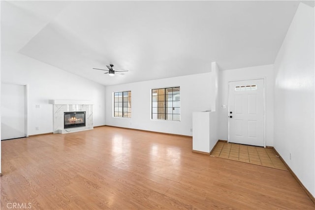 unfurnished living room with a ceiling fan, light wood finished floors, vaulted ceiling, and a fireplace