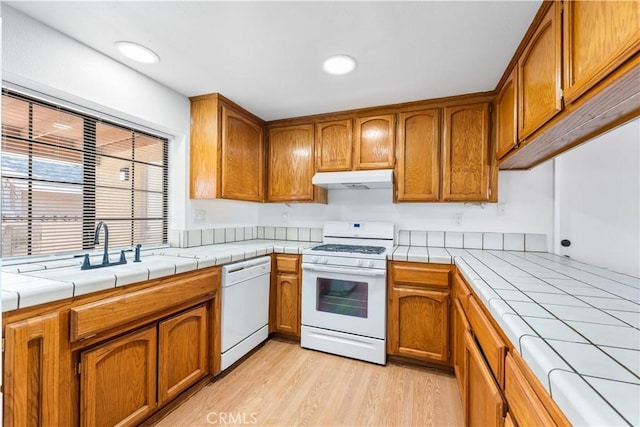 kitchen featuring white appliances, tile counters, under cabinet range hood, and brown cabinetry