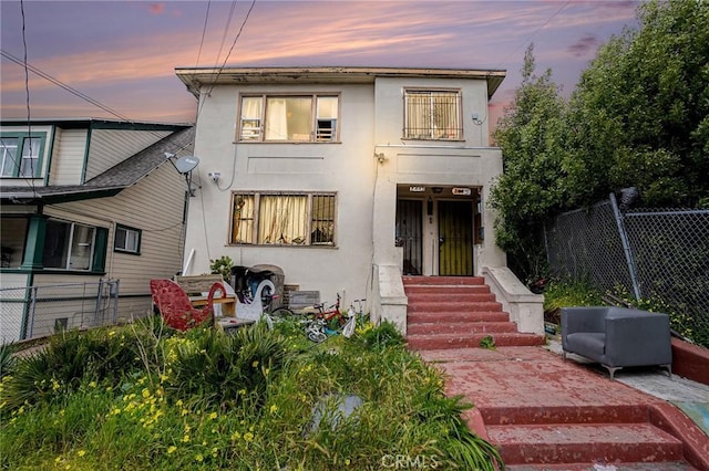 back of house at dusk with entry steps, stucco siding, and fence