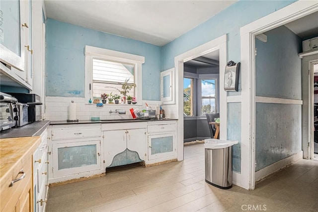 kitchen featuring dark countertops, tasteful backsplash, light wood-type flooring, a sink, and white cabinets