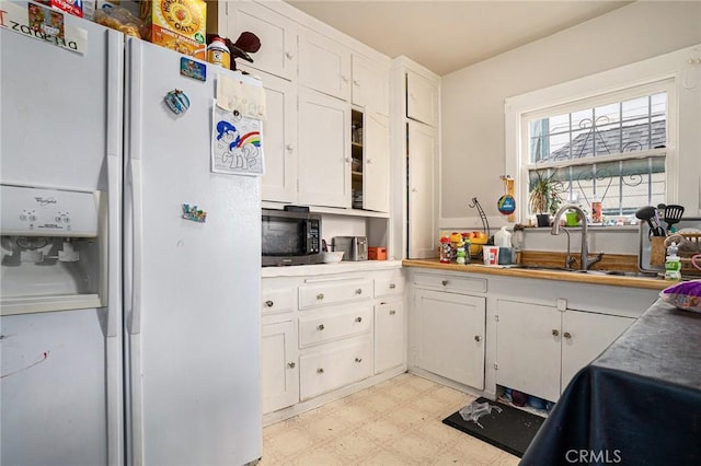 kitchen with white cabinets, a sink, white refrigerator with ice dispenser, and light floors
