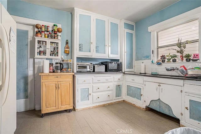 kitchen featuring white refrigerator, light wood-style flooring, black microwave, and glass insert cabinets