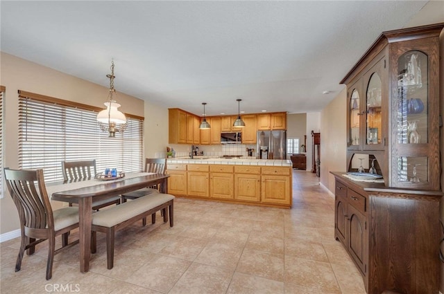 interior space featuring stainless steel appliances, decorative light fixtures, tile countertops, baseboards, and glass insert cabinets