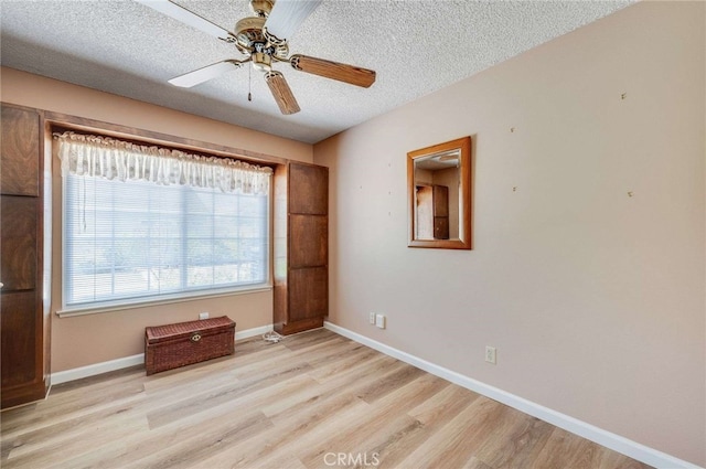 empty room with a ceiling fan, a textured ceiling, baseboards, and light wood-type flooring