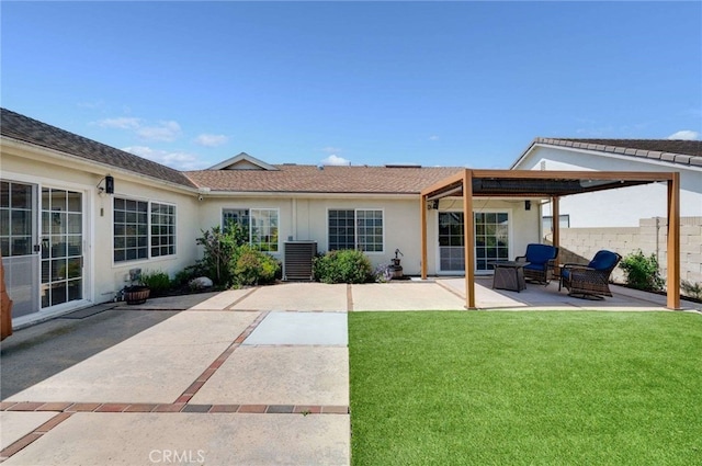 rear view of property with fence, stucco siding, a yard, and a patio area