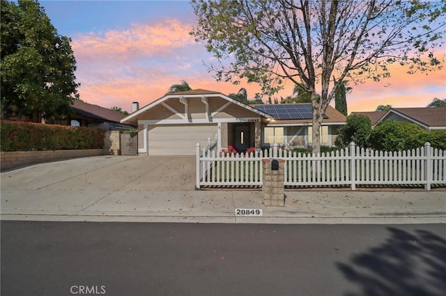 view of front of house featuring a fenced front yard, an attached garage, stucco siding, roof mounted solar panels, and concrete driveway