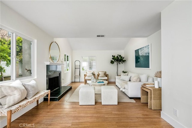 living area featuring visible vents, light wood-style floors, vaulted ceiling, and a premium fireplace