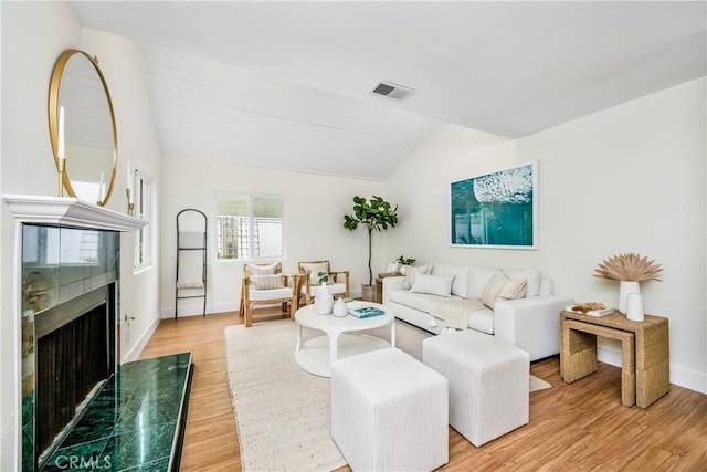 living room featuring visible vents, a fireplace, baseboards, light wood-style flooring, and vaulted ceiling