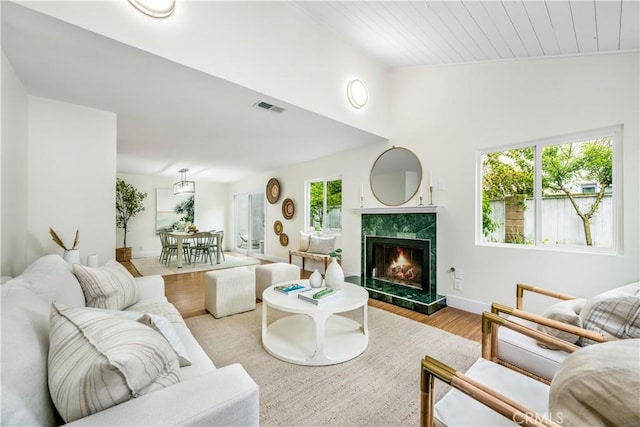 living room featuring a premium fireplace, baseboards, wooden ceiling, wood finished floors, and visible vents
