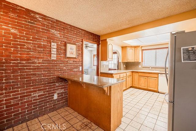 kitchen featuring brick wall, light tile patterned floors, freestanding refrigerator, a peninsula, and a breakfast bar