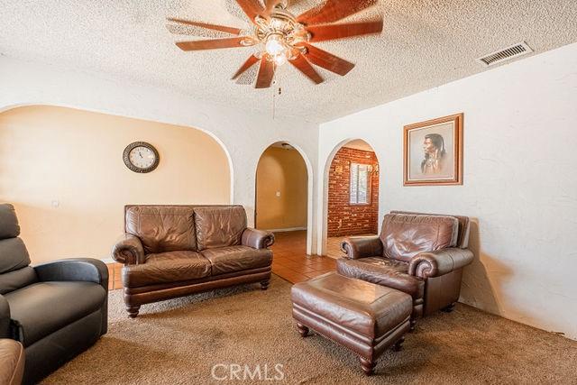 living area featuring arched walkways, a textured ceiling, visible vents, and ceiling fan