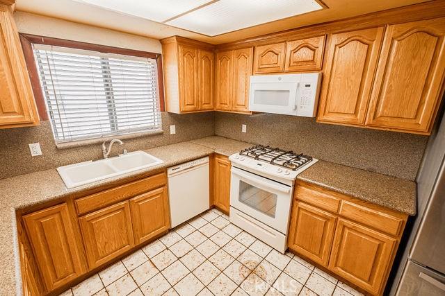 kitchen with brown cabinetry, backsplash, a sink, light countertops, and white appliances