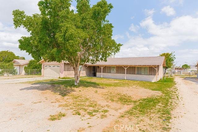 ranch-style home with a garage, dirt driveway, and fence