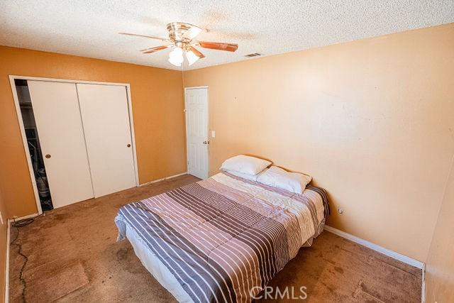 bedroom featuring carpet flooring, a textured ceiling, a ceiling fan, visible vents, and a closet