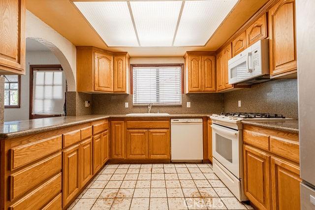 kitchen featuring brown cabinetry, a sink, decorative backsplash, and white appliances