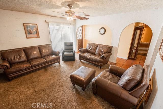 carpeted living room with arched walkways, ceiling fan, a textured wall, and a textured ceiling