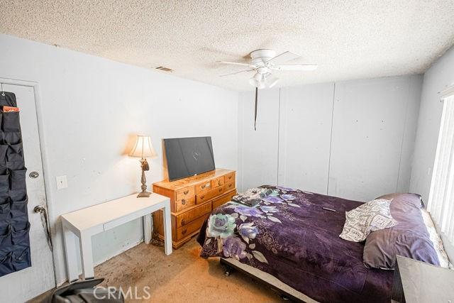 carpeted bedroom with a textured ceiling, visible vents, and ceiling fan
