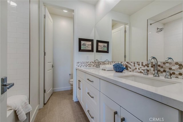 bathroom featuring double vanity, a sink, toilet, and tasteful backsplash