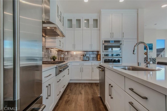 kitchen with wall chimney range hood, light countertops, white cabinets, a sink, and appliances with stainless steel finishes