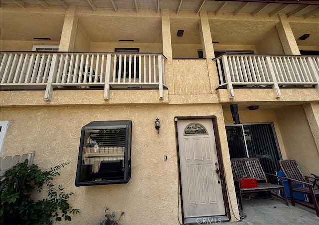 view of exterior entry with stucco siding and a balcony