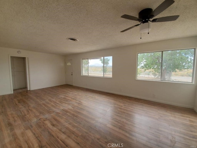 empty room with a ceiling fan, a textured ceiling, visible vents, wood finished floors, and baseboards