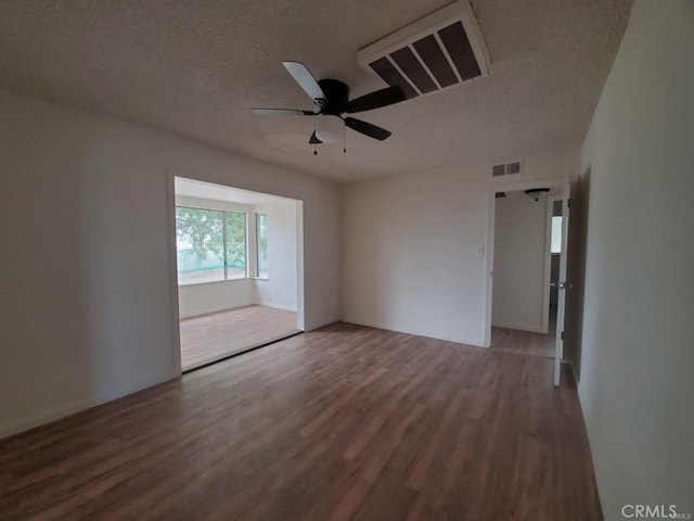 empty room featuring a textured ceiling, ceiling fan, wood finished floors, and visible vents