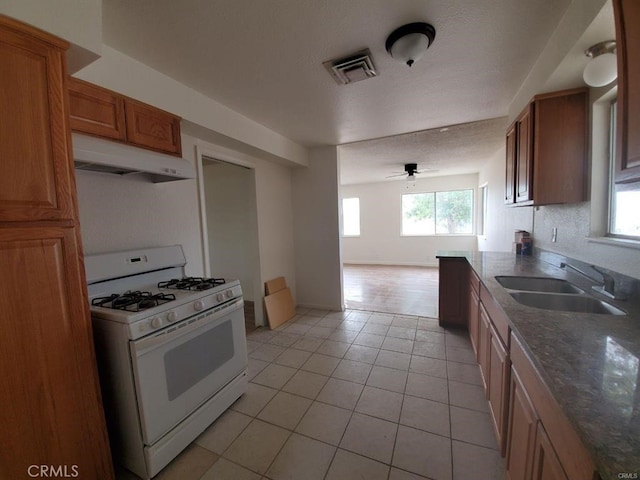 kitchen with a sink, white gas stove, light tile patterned floors, under cabinet range hood, and visible vents