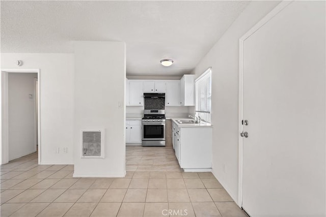 kitchen with stainless steel gas range, light tile patterned flooring, a sink, light countertops, and white cabinetry