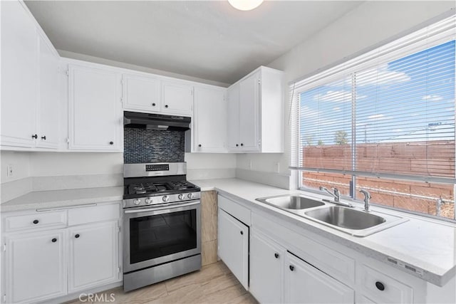 kitchen with under cabinet range hood, white cabinets, a sink, and stainless steel gas stove