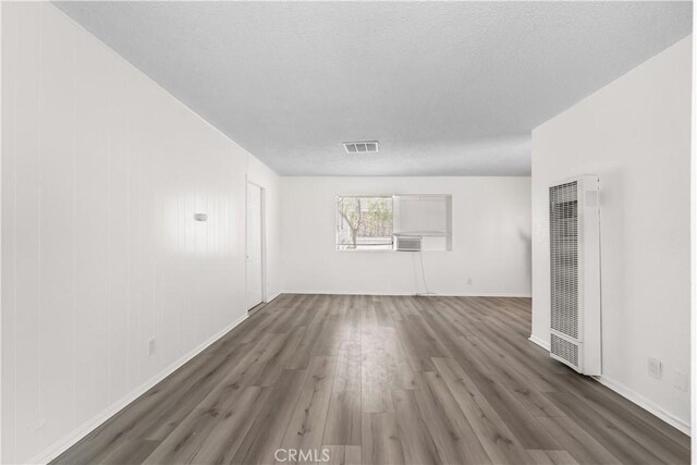 unfurnished living room with a textured ceiling, a heating unit, baseboards, wood finished floors, and visible vents
