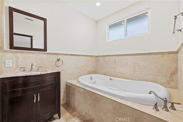 full bathroom featuring vanity, a wainscoted wall, a bath, and tile walls