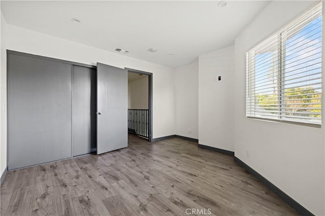 unfurnished bedroom featuring baseboards, visible vents, wood finished floors, and a closet