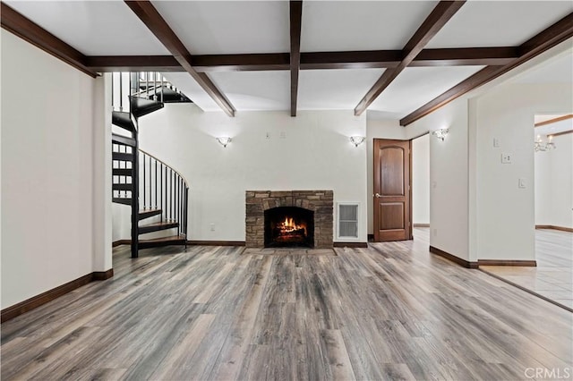 unfurnished living room with a fireplace, stairs, baseboards, wood finished floors, and beamed ceiling