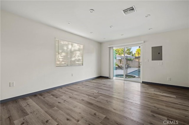 spare room featuring baseboards, electric panel, wood finished floors, and visible vents