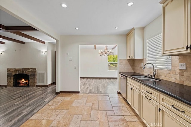 kitchen with cream cabinets, dark countertops, a sink, dishwasher, and backsplash