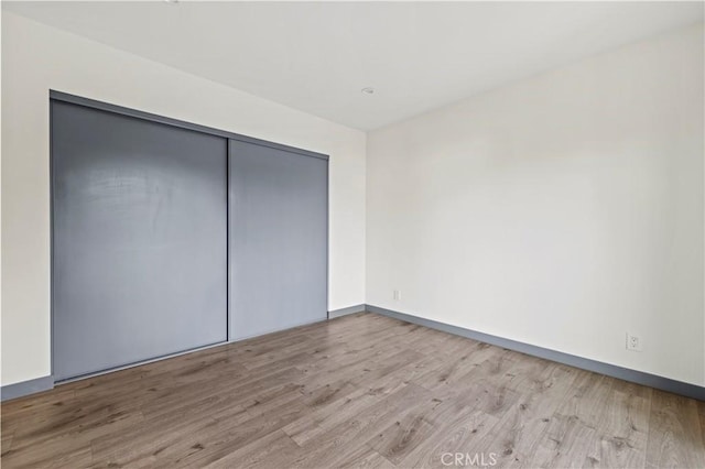 unfurnished bedroom featuring baseboards, wood finished floors, and a closet