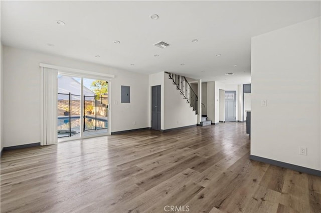 unfurnished living room with baseboards, electric panel, and wood finished floors