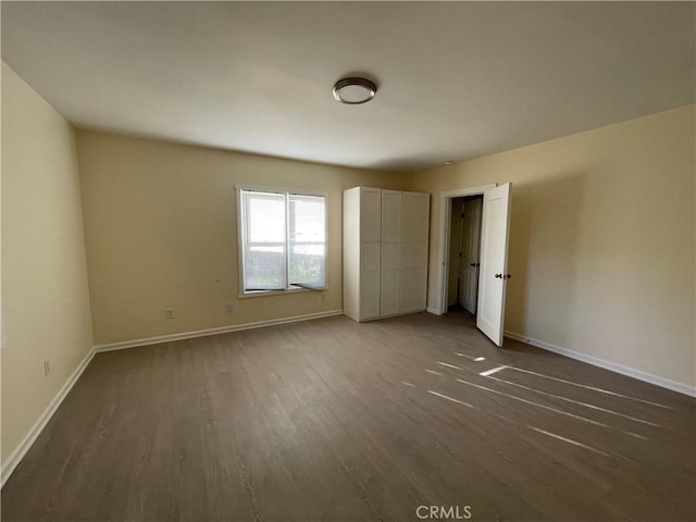 unfurnished bedroom featuring baseboards and dark wood-type flooring