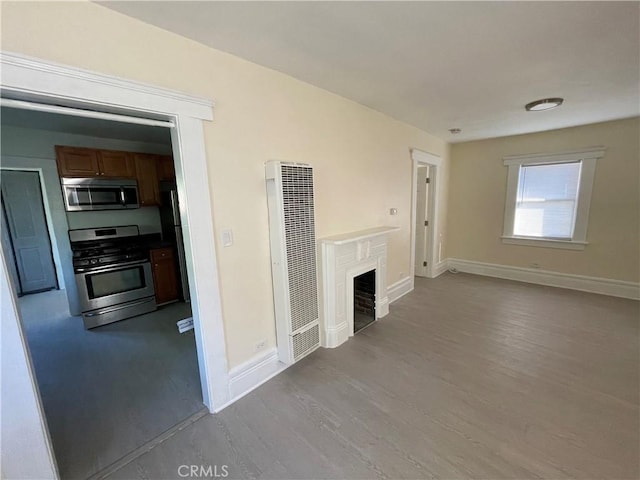 unfurnished living room with baseboards, a fireplace, wood finished floors, and a heating unit