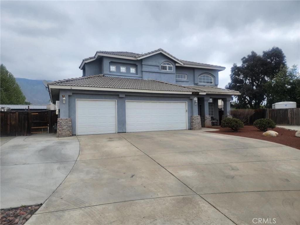 traditional home featuring fence, stucco siding, concrete driveway, and stone siding