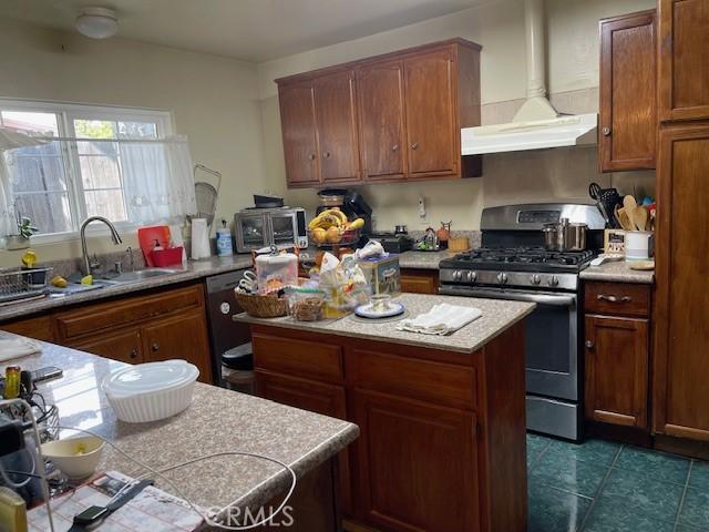 kitchen featuring wall chimney range hood, stainless steel gas stove, light countertops, a center island, and dark tile patterned floors