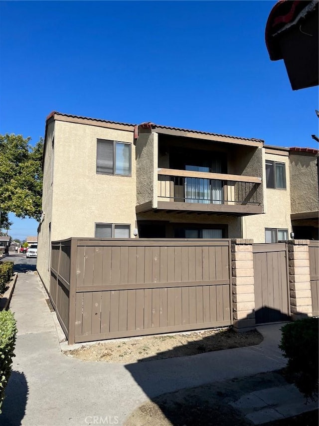view of front of property with stucco siding, a balcony, a tile roof, and fence