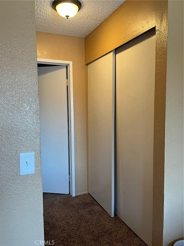 hall featuring carpet floors and a textured wall